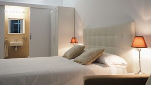 Hotellihuone, jossa on sänky, kaksi yöpöytävalaisinta, sängynpääty sekä kylpyhuone, jossa on peili ja pesuallas.