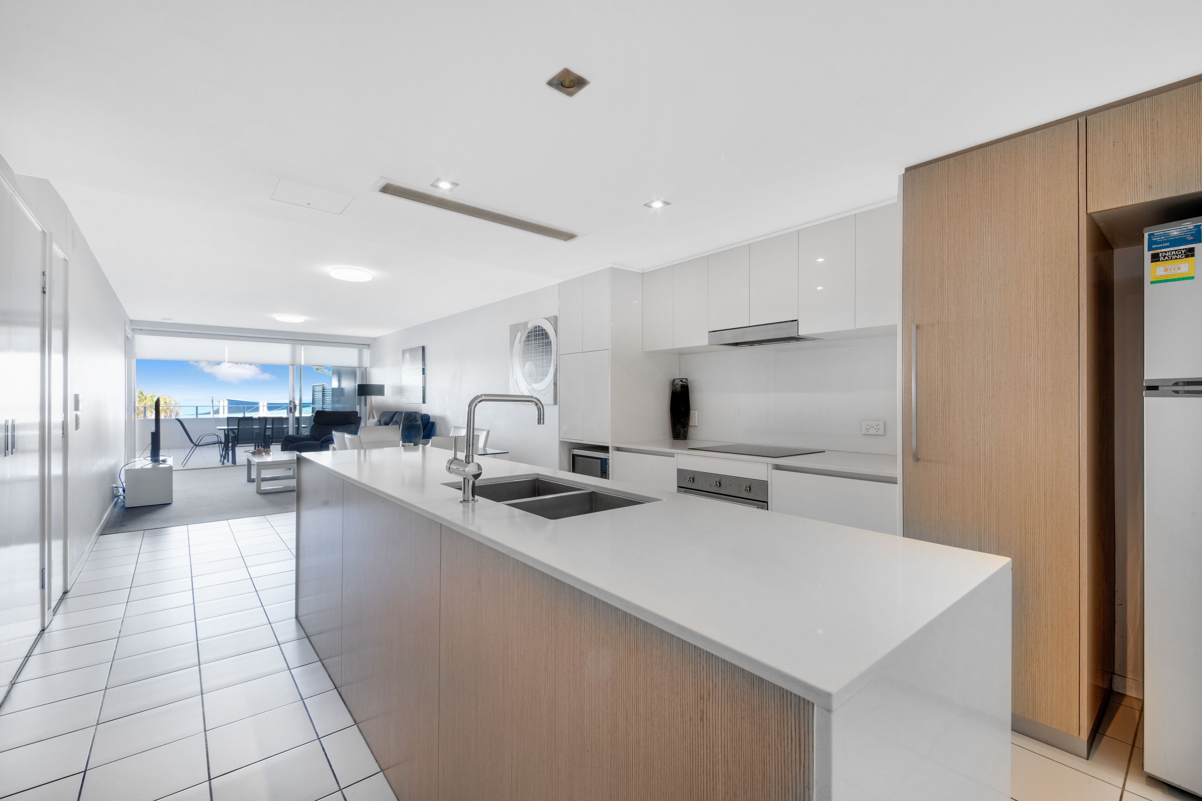 A modern kitchen with a large island, white cabinetry, and a view to the outdoors.