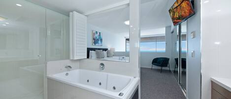Une salle de bain moderne dotée d’une grande baignoire, d’une douche en verre et offrant une vue sur l’espace de vie grâce à une porte ouverte.