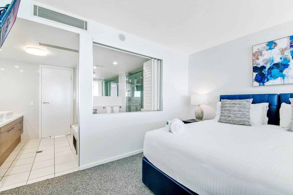 Habitación de hotel moderna con una cama grande, un baño con ducha de vidrio y vistas a la ciudad.