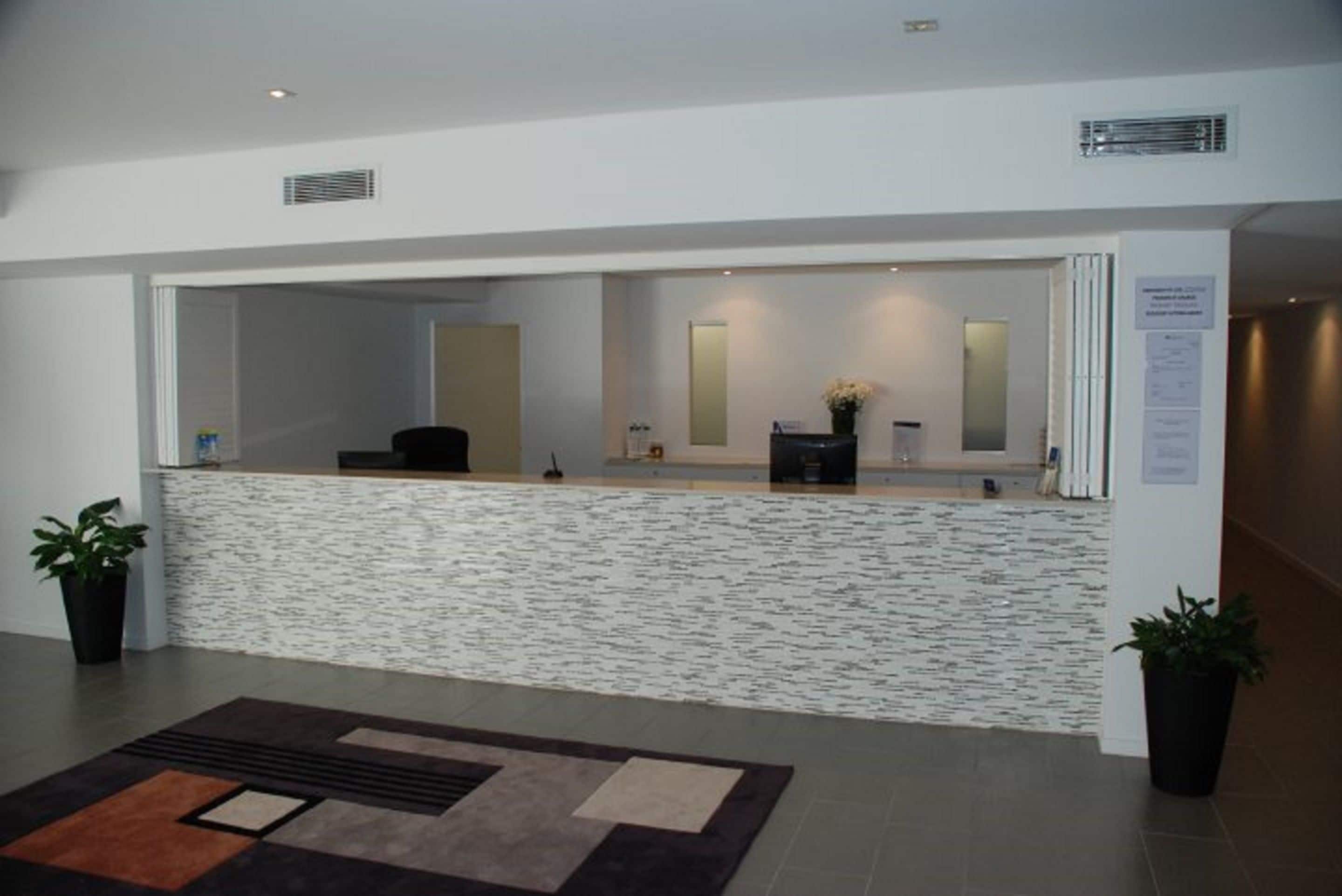 A reception area with a stone counter, two potted plants, a mirror, and a bulletin board.