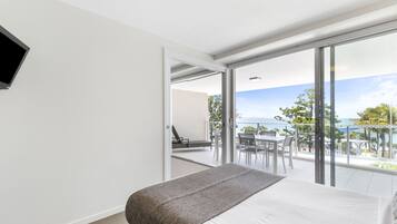 A bedroom with a bed, a TV mounted on the wall, and a balcony with a table and chairs.