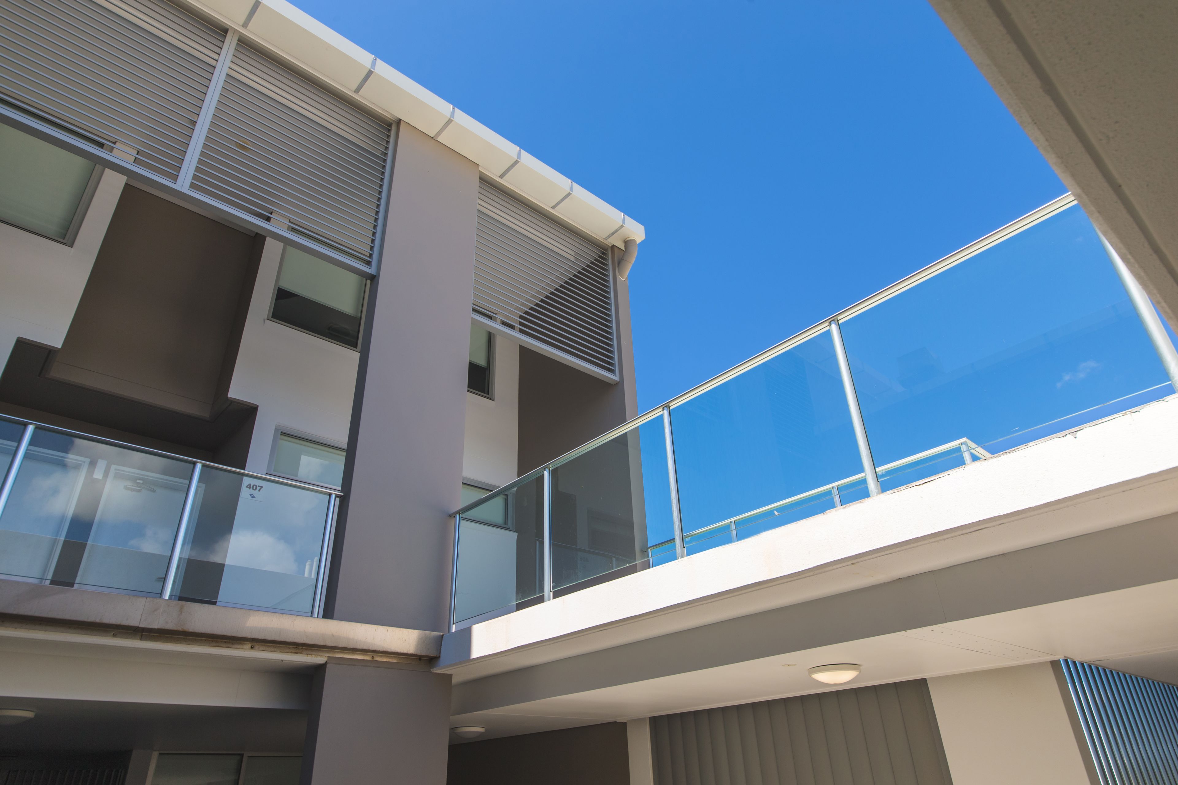 Un immeuble à plusieurs étages doté de balcons, de grandes fenêtres et surplombant un ciel d’un bleu éclatant.