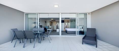 Una habitación de hotel moderna con balcón, una zona de comedor con sillas y una mesa, y una cama.