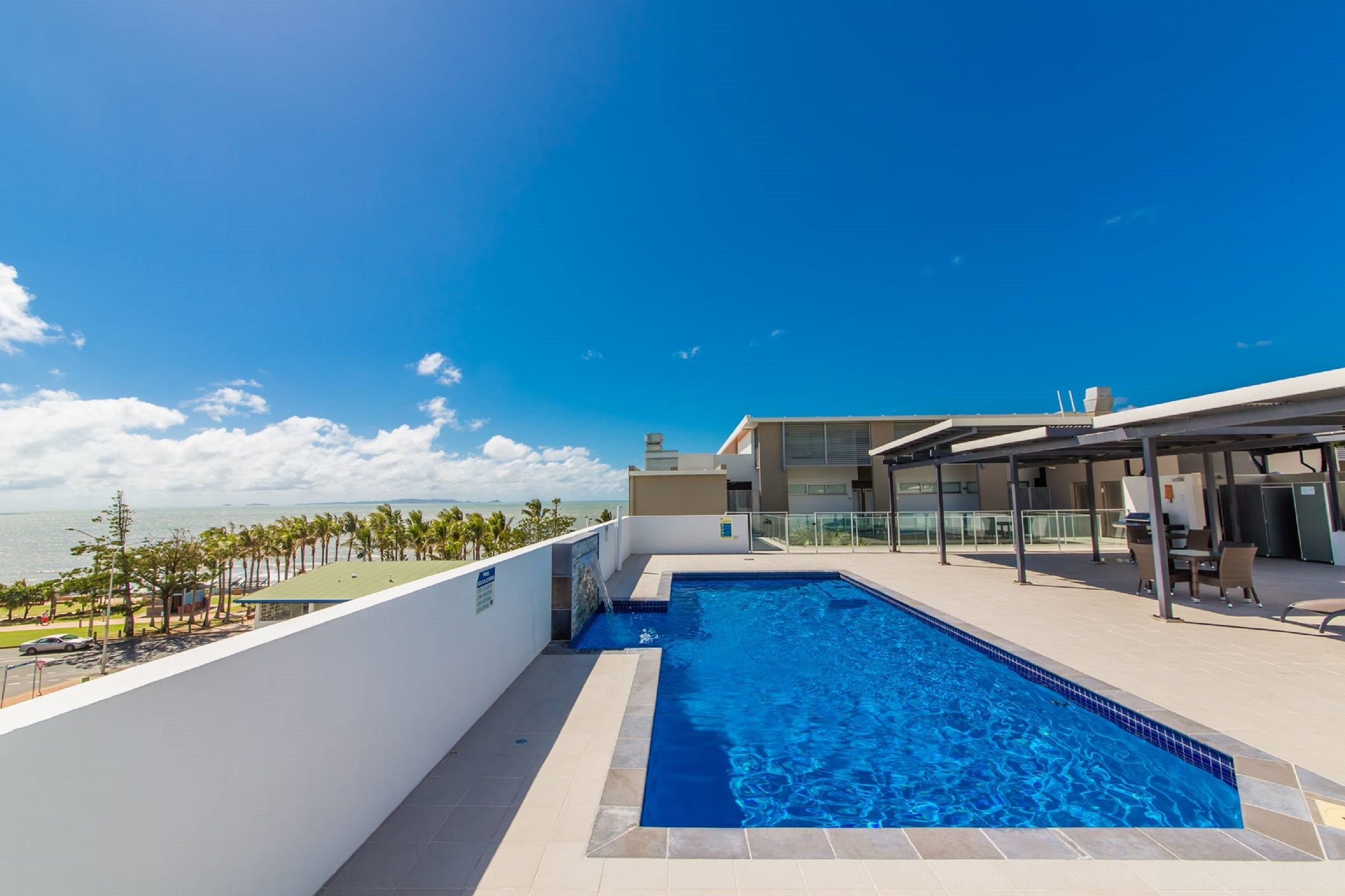 A rooftop swimming pool with a view of the ocean and palm trees.
