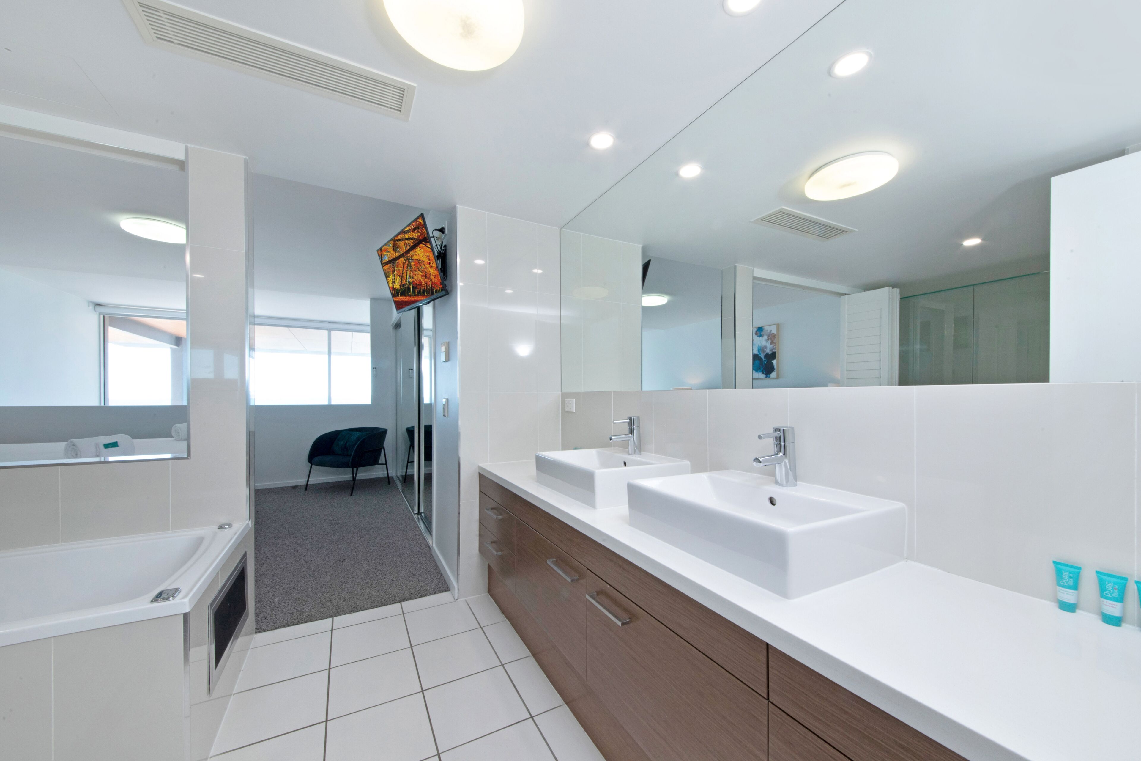 Un baño moderno con dos lavamanos, una bañera y un espejo grande.