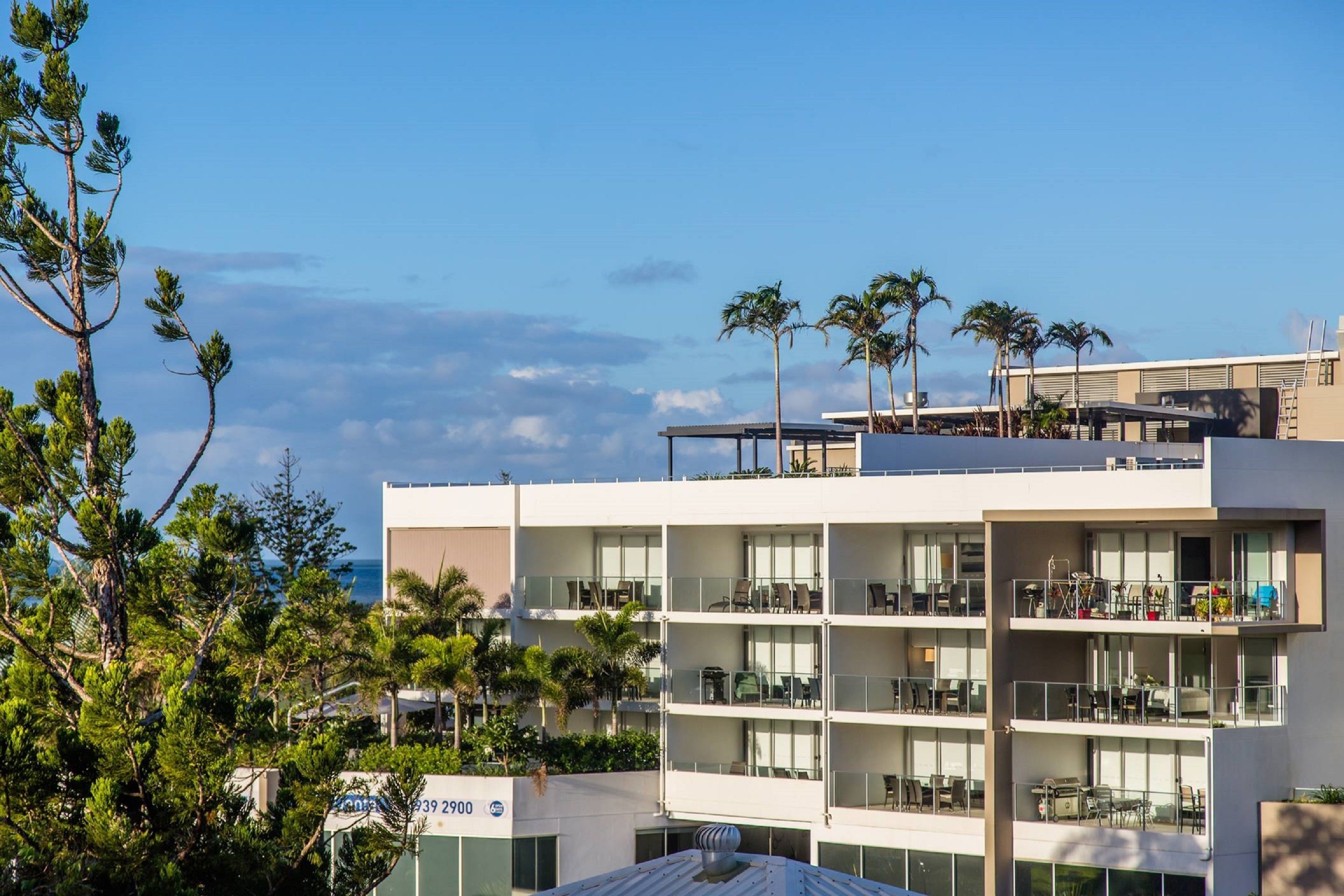 A multi-story hotel with balconies, large windows, and palm trees.