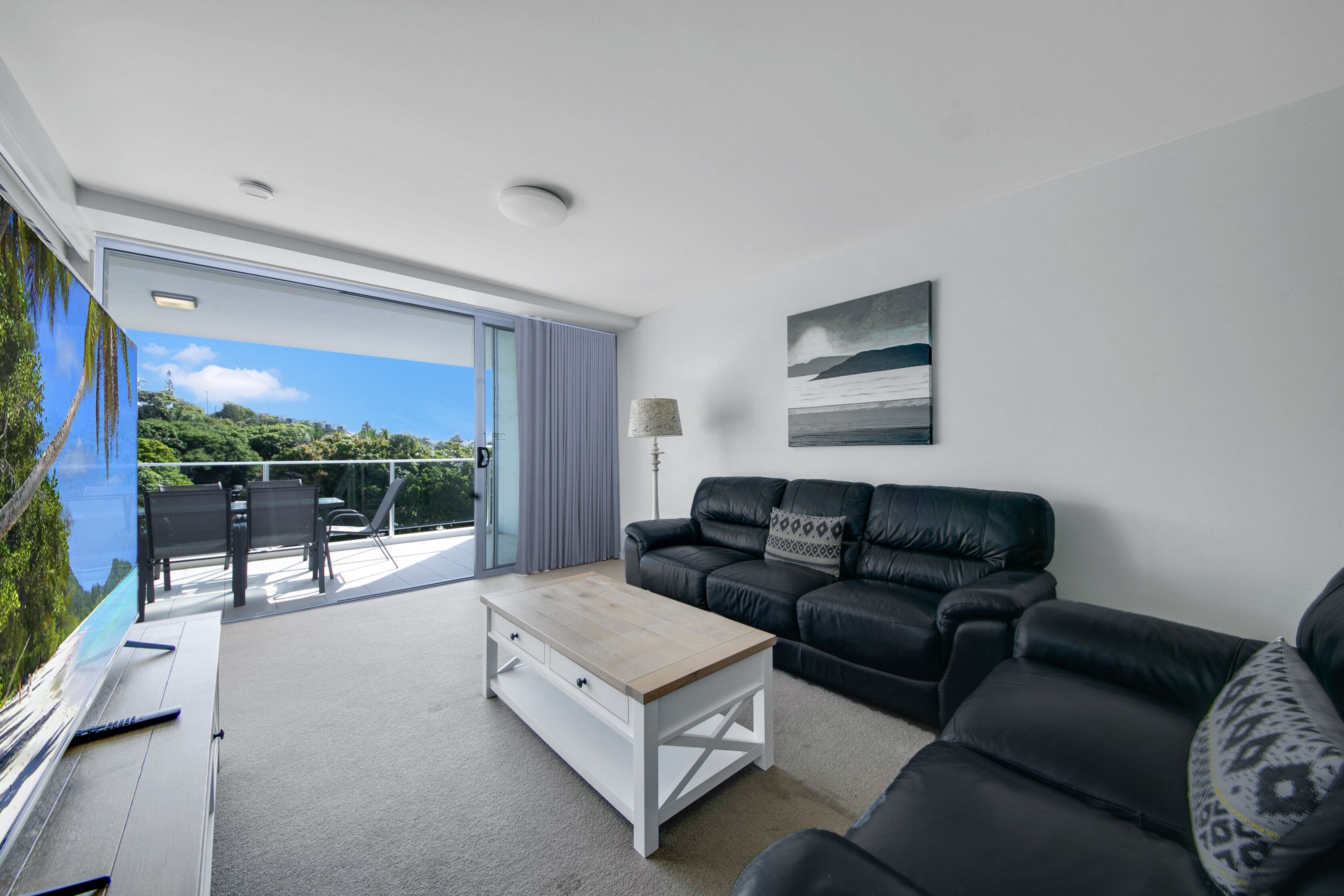 A modern living room with a black leather sofa, a white coffee table, and a painting on the wall.