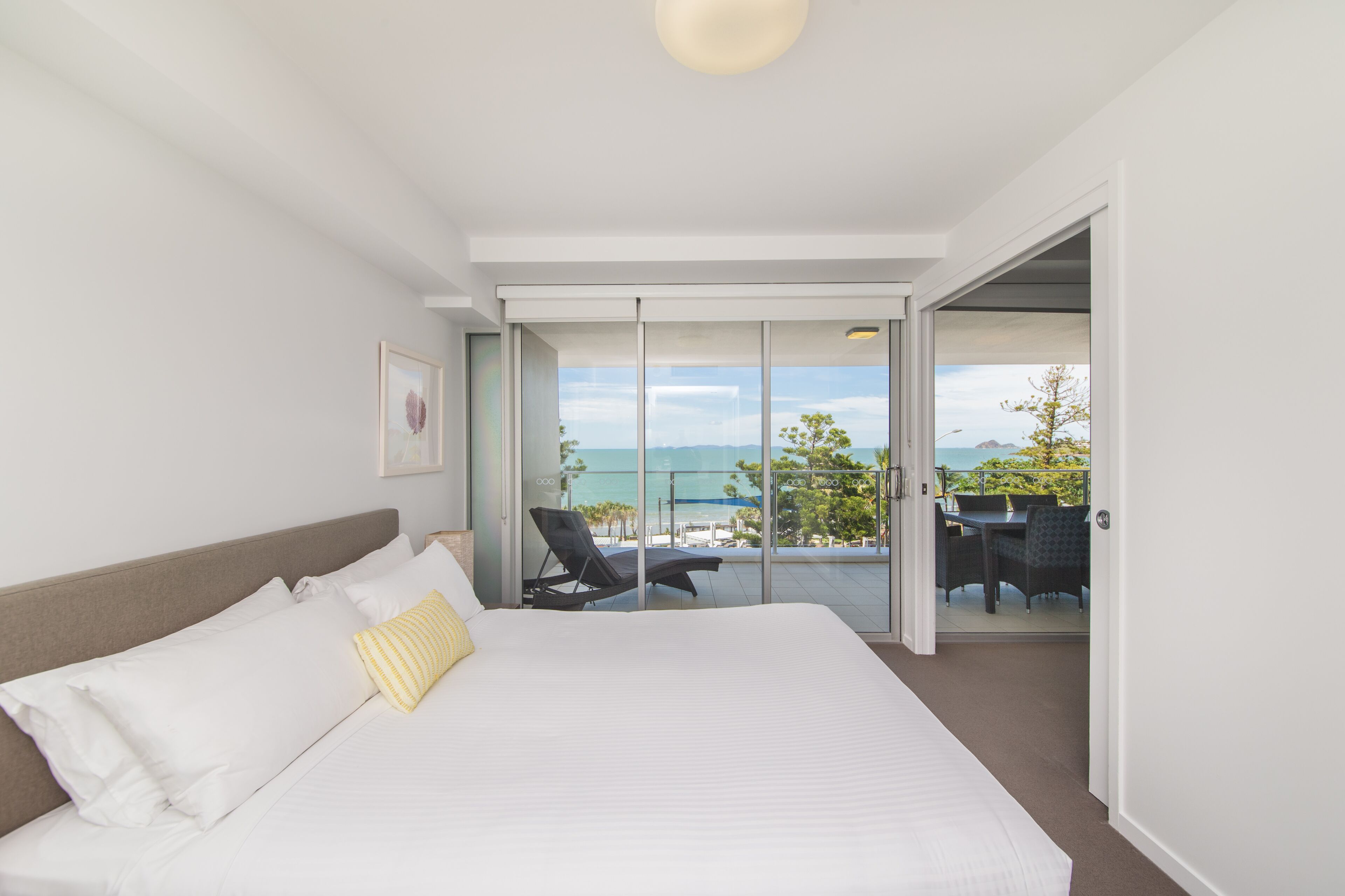 A hotel room with a large bed, a balcony with a view of the sea, and a dining area with outdoor furniture.