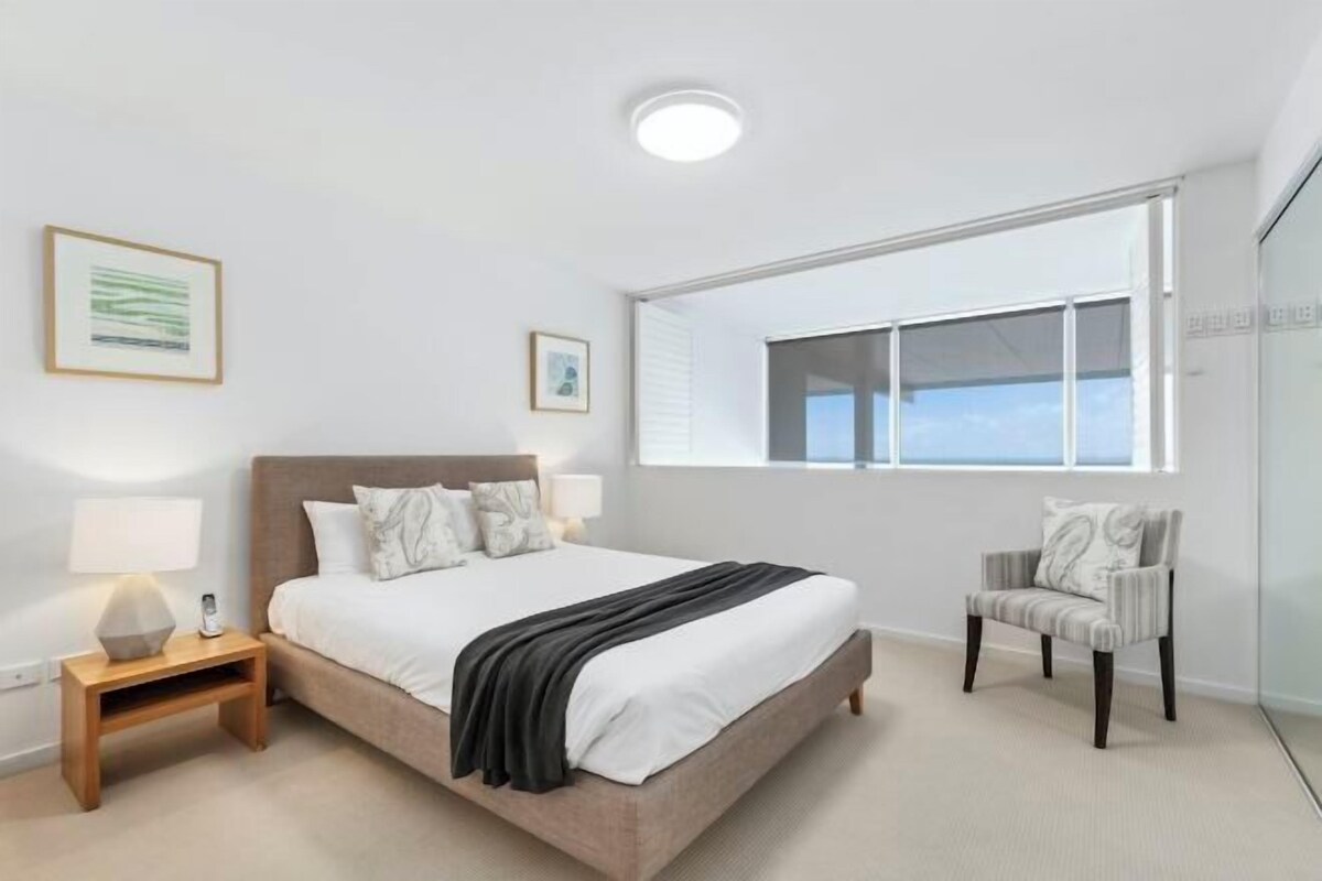 A bedroom with a bed, bedside tables, a chair, and a window.