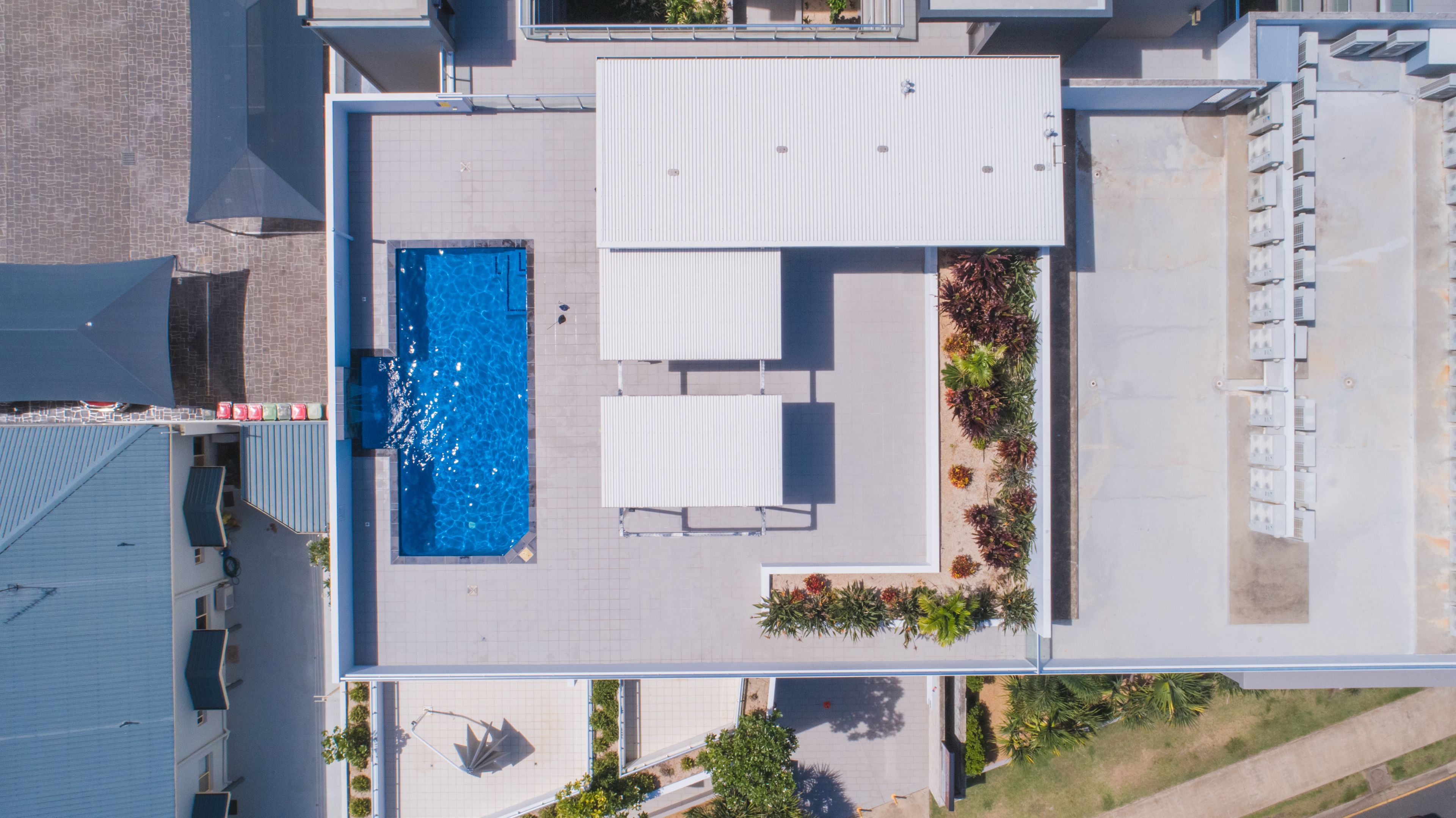An aerial view of a rooftop with a swimming pool, sun loungers, and a garden area.