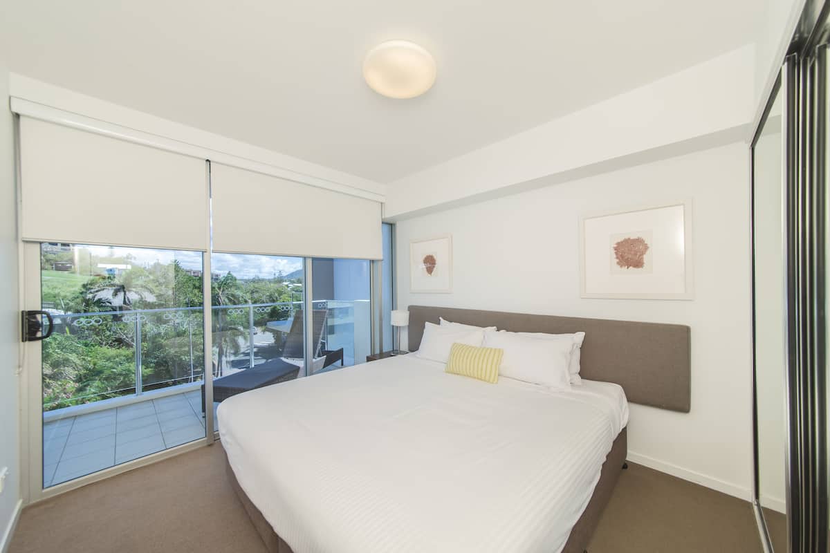 Una habitación de hotel moderna con una cama grande, un balcón con puerta de vidrio y dos cuadros en la pared.
