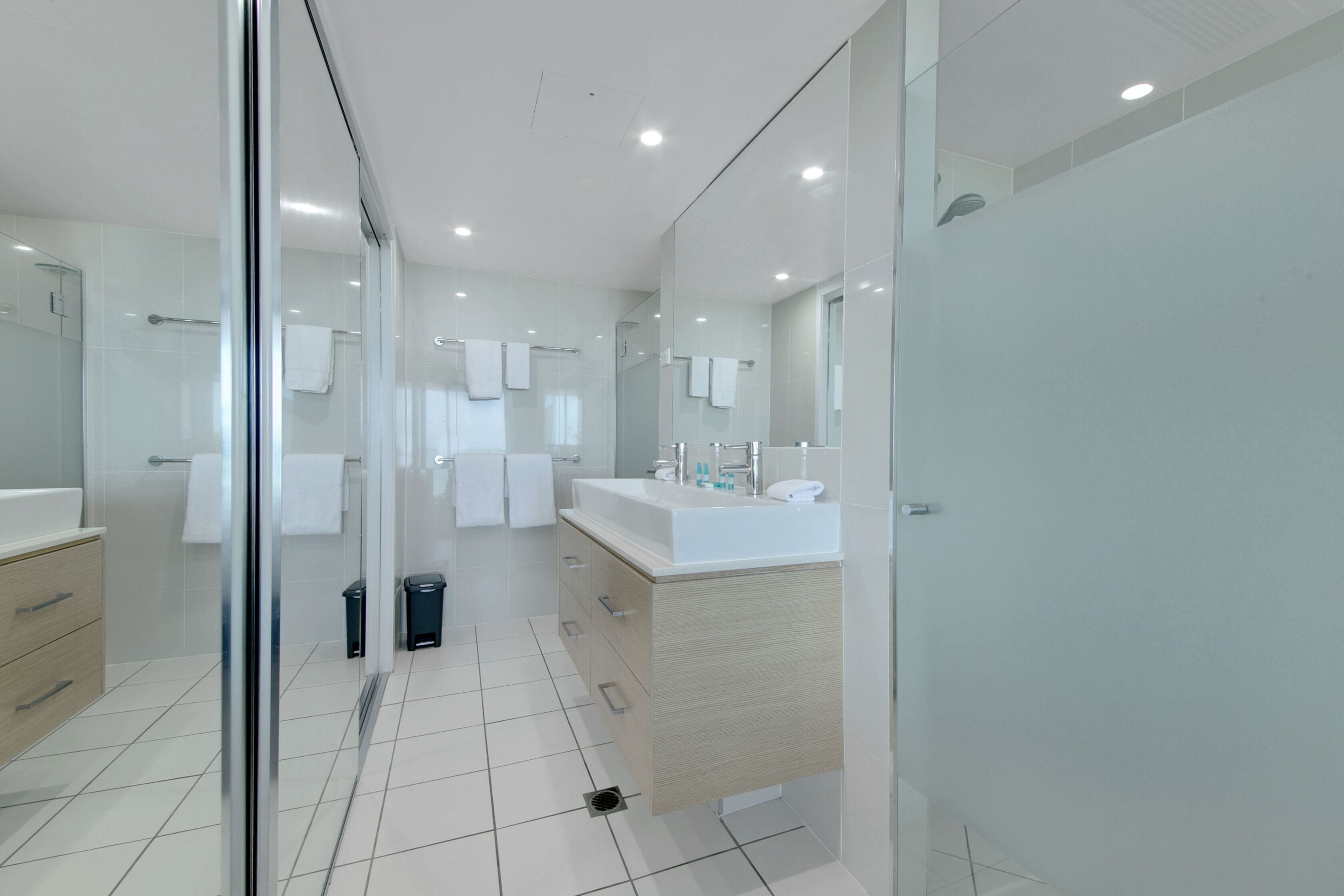 A modern bathroom with a glass shower enclosure, a large mirror, and a white sink with a wooden vanity.