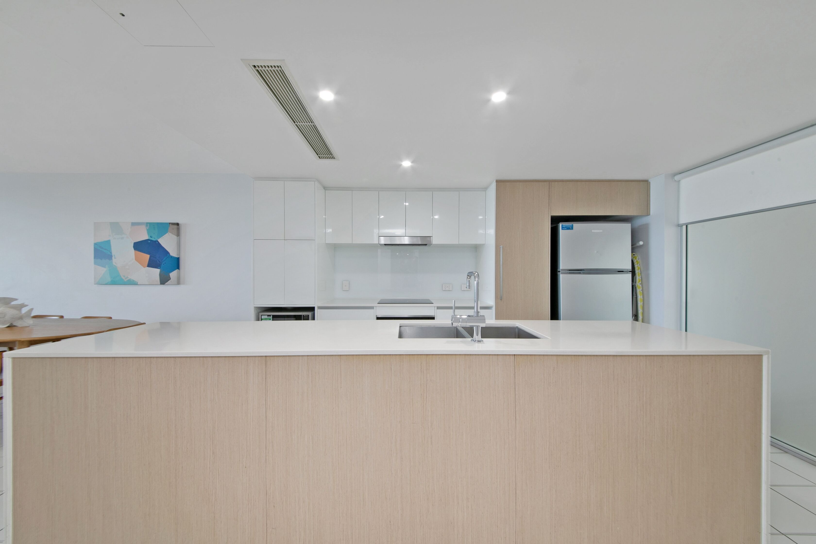 A modern kitchen with white cabinetry, a central island with a sink, and a stainless steel range hood.