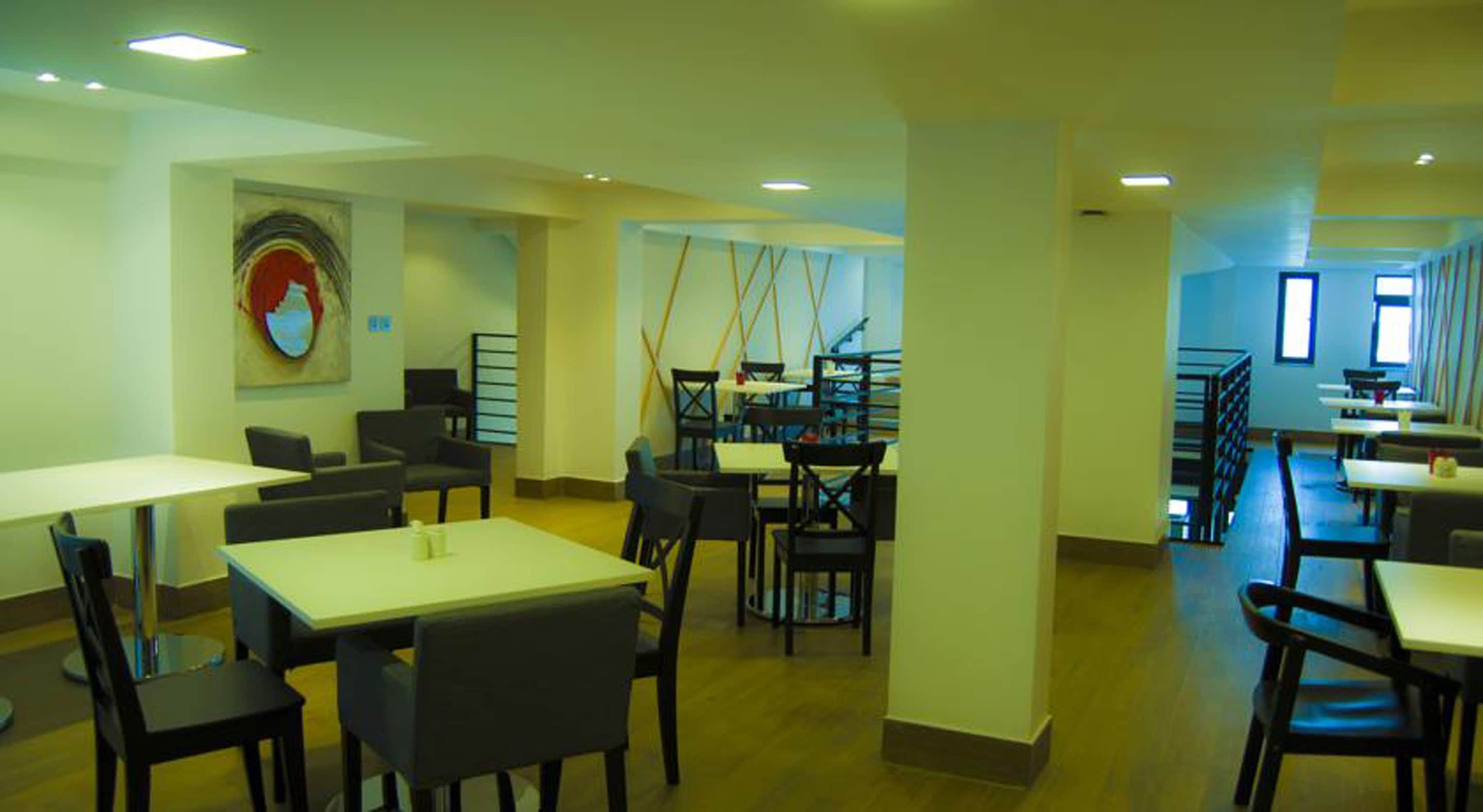 A spacious dining area with multiple tables and chairs, a staircase, and a large window providing natural light.