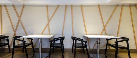 A modern dining area with four tables and chairs, wooden wall accents, and recessed ceiling lighting.