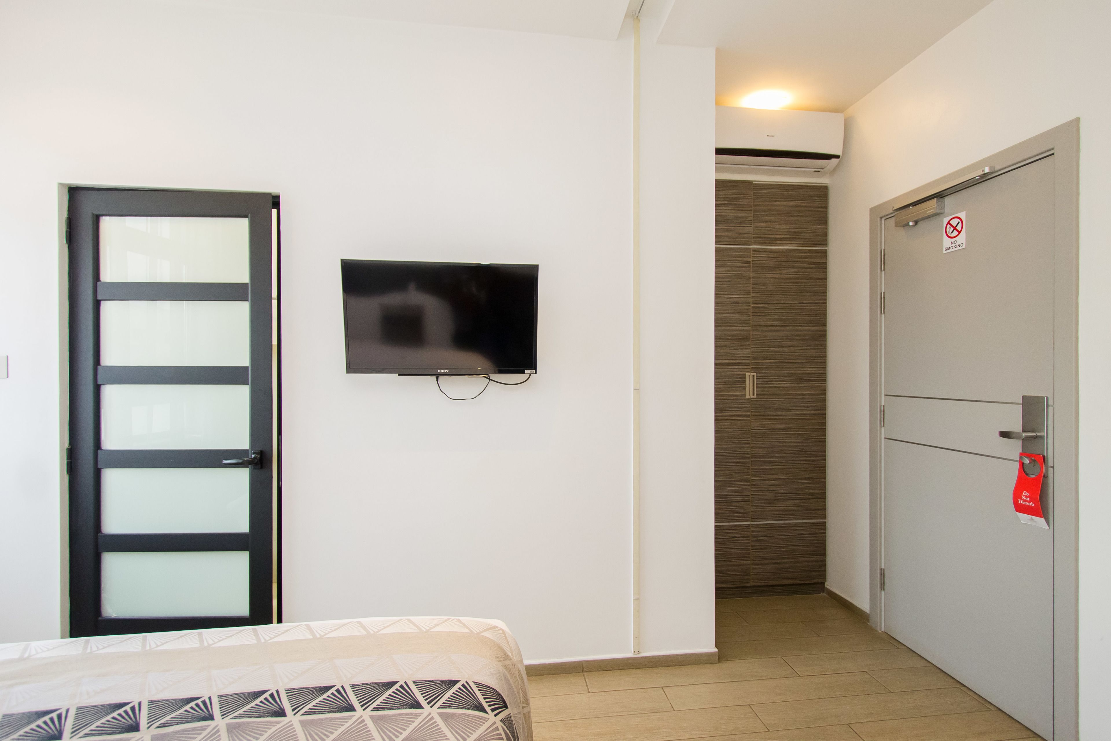 A hotel room with a bed, a television, a wardrobe, and a door.