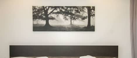 A hotel room with two beds, a headboard, and a wall-mounted artwork of trees.