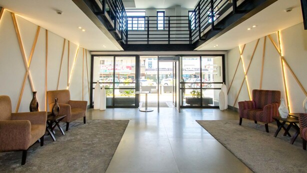 A spacious lobby with a high ceiling, a central staircase, and a view of the street through large glass doors. - Imperial Hotel Express (Kisumu)