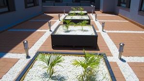 A courtyard with rectangular planters containing plants, surrounded by a tiled walkway and a building with windows and a balcony. - Imperial Hotel Express (Kisumu)