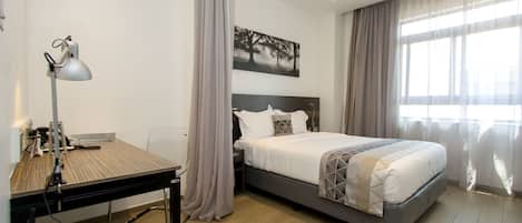 A modern hotel room with a bed, a desk, and a computer.