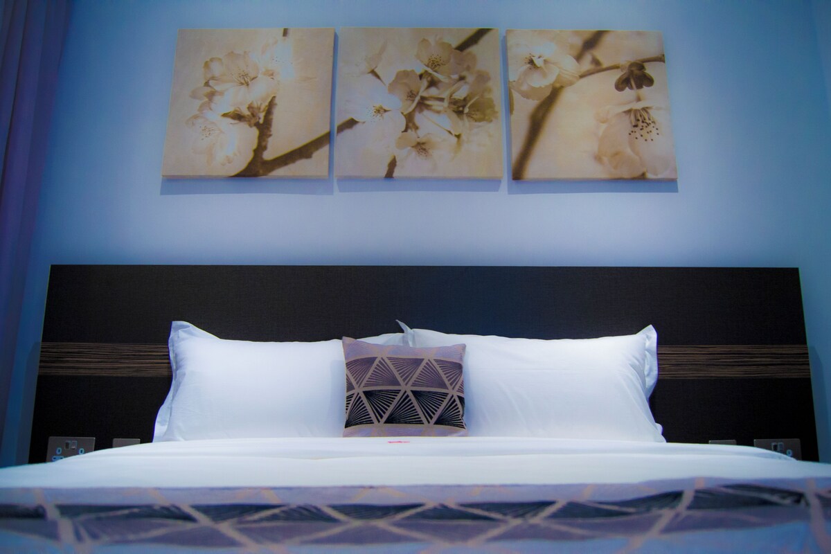 A hotel room with a bed, a headboard, and three wall-mounted floral paintings.