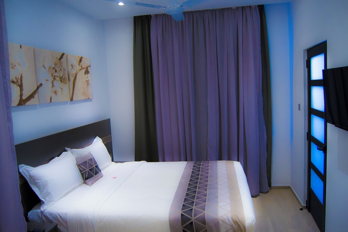 Une chambre d’hôtel avec un lit, des rideaux, un ventilateur de plafond et des œuvres d’art accrochées au mur.
