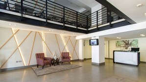 A modern lobby with a reception desk, seating area with chairs, a staircase, and a TV screen. - Imperial Hotel Express (Kisumu)
