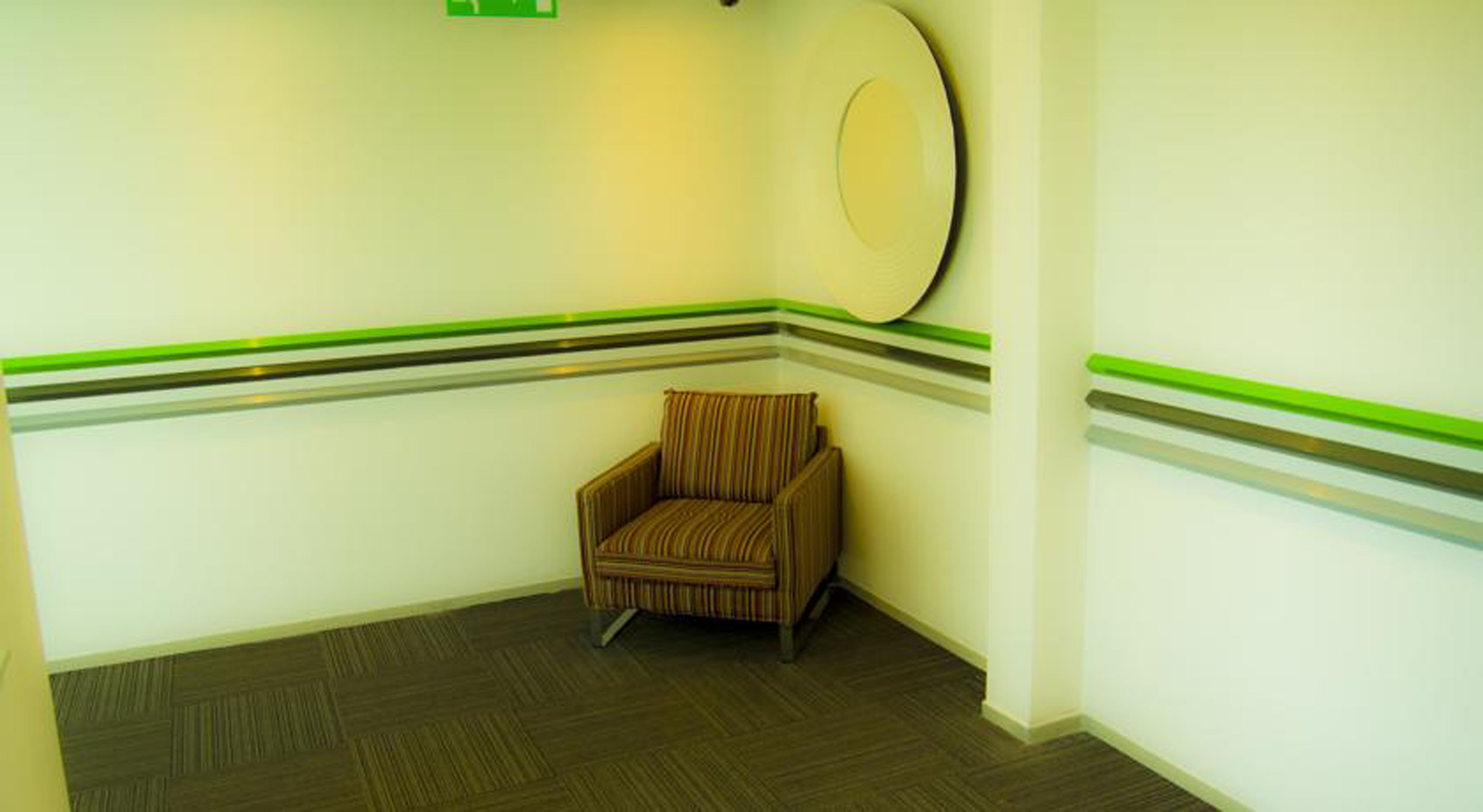 A corner room with a striped chair, a round mirror on the wall, and green stripes along the baseboards.