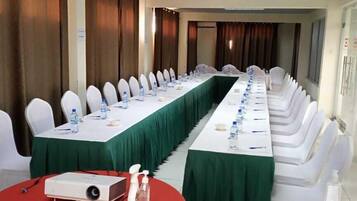 A conference room with long tables, white chairs, and a projector on a red table.