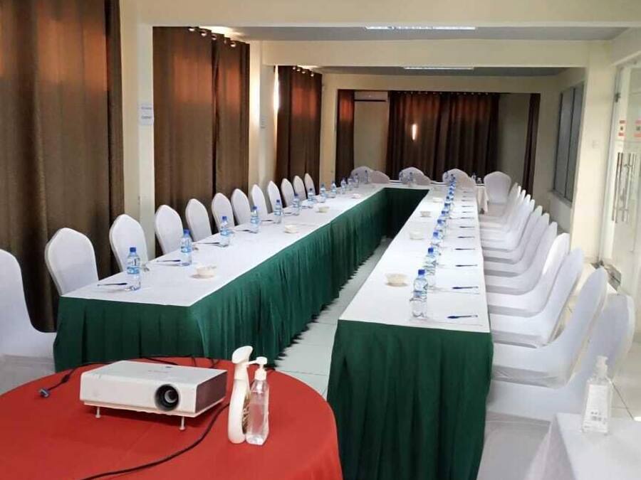 A conference room with long tables, white chairs, and a projector on a red table.