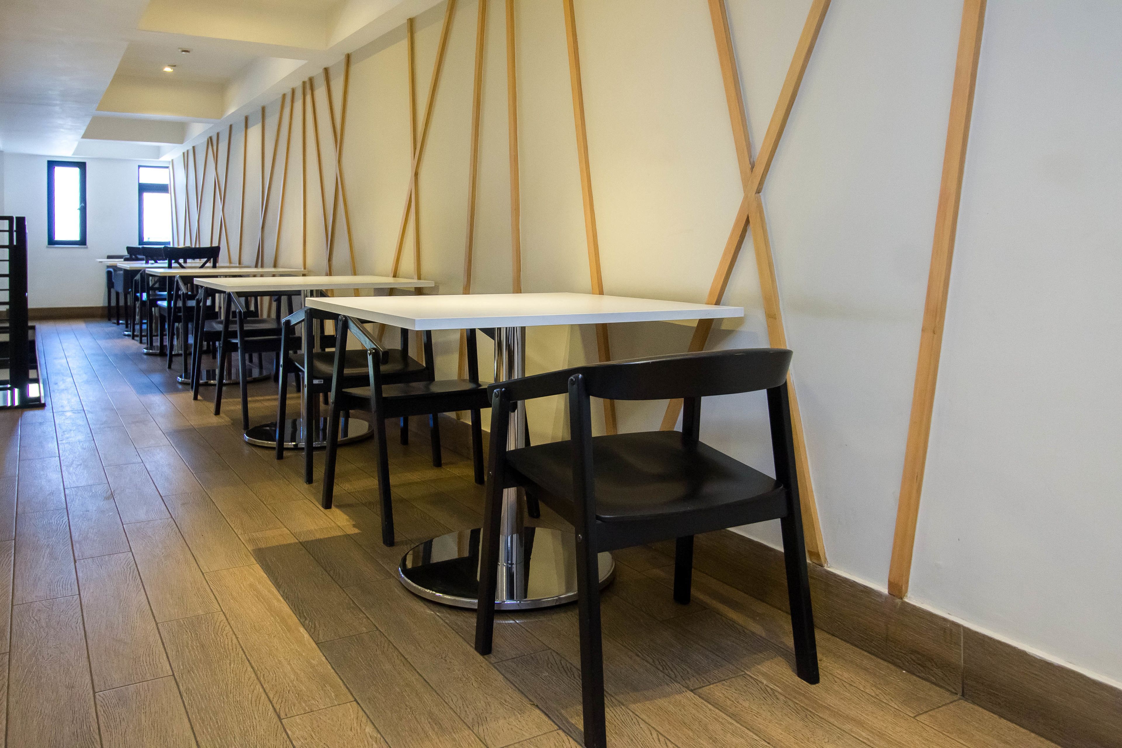 A modern dining area with long tables and black chairs, wooden paneling on the walls, and a wooden floor.