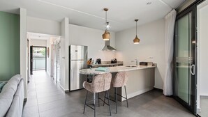 Une cuisine moderne dotée d’un îlot central, de tabourets de bar, d’appareils électroménagers en acier inoxydable et de luminaires suspendus.