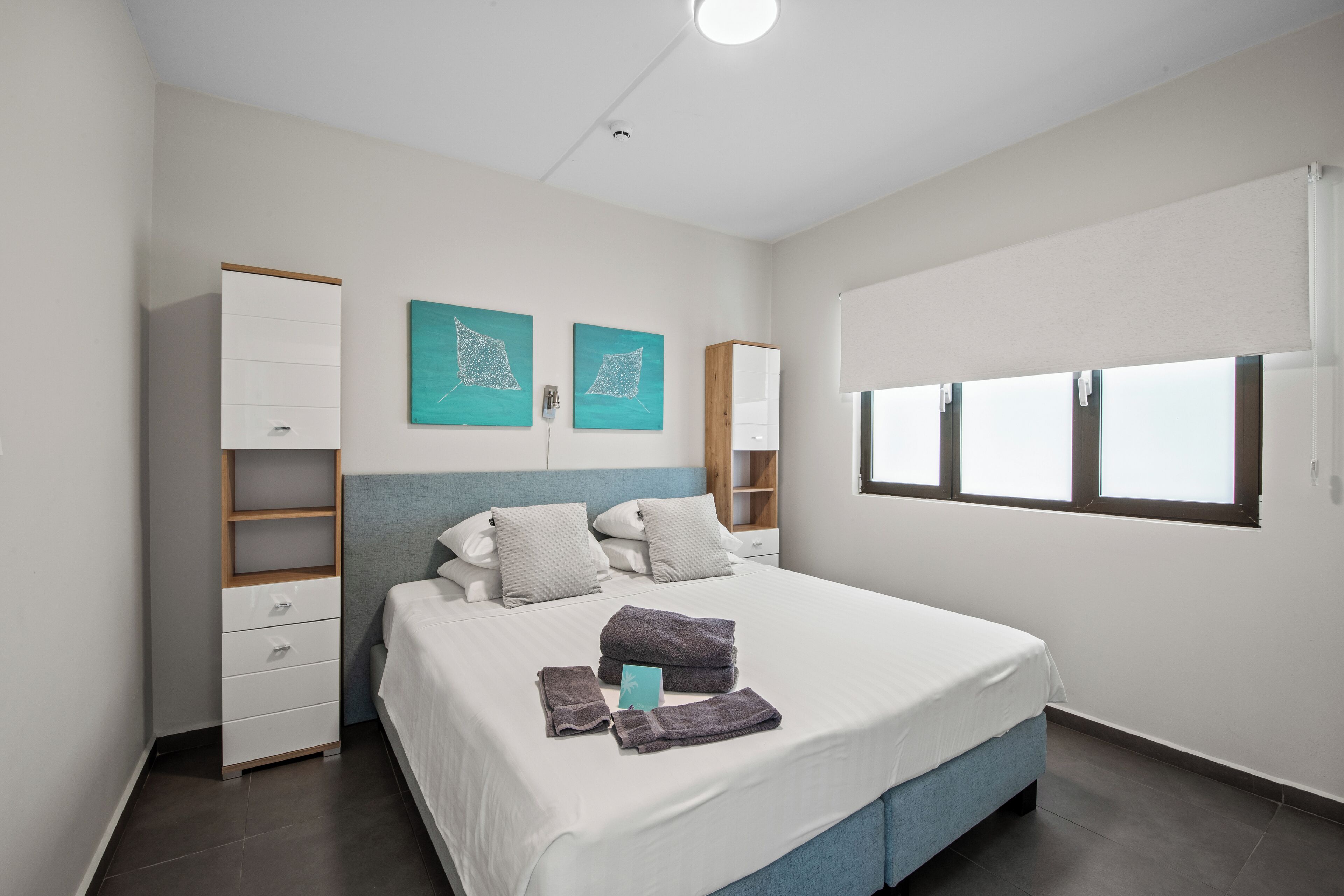 Ein modernes Schlafzimmer mit einem großen Bett, einem Kleiderschrank, zwei Wandregalen und einem Fenster mit Jalousien.