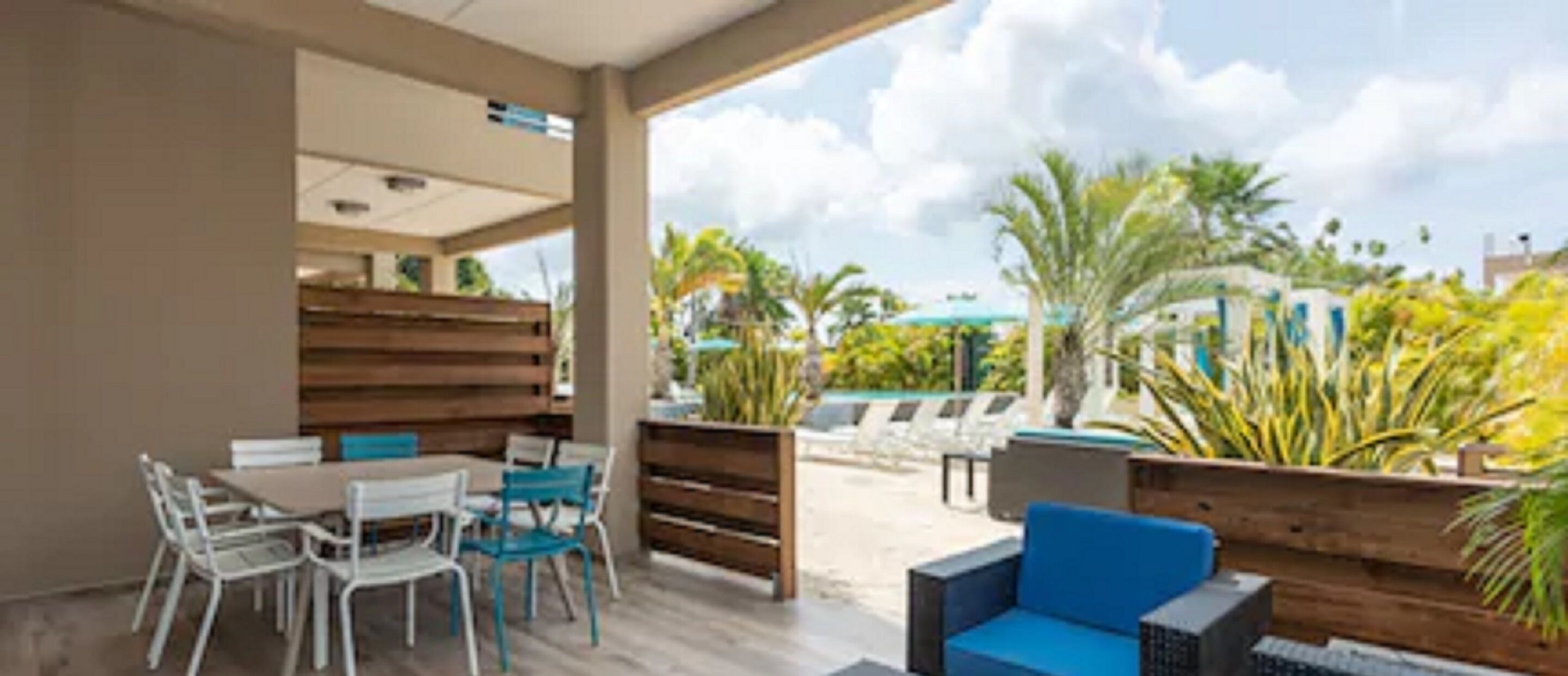 An outdoor seating area with a wooden bench and a table, surrounded by chairs.