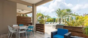 An outdoor seating area with a wooden bench and a table, surrounded by chairs. - The Beach House Curacao (Willemstad)
