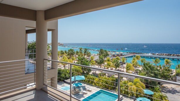 Un balcon avec vue sur une plage, une piscine et une jetée.