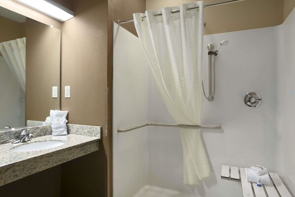 A bathroom with a granite countertop sink, a mirror, a shower with a curtain, and a towel rack.