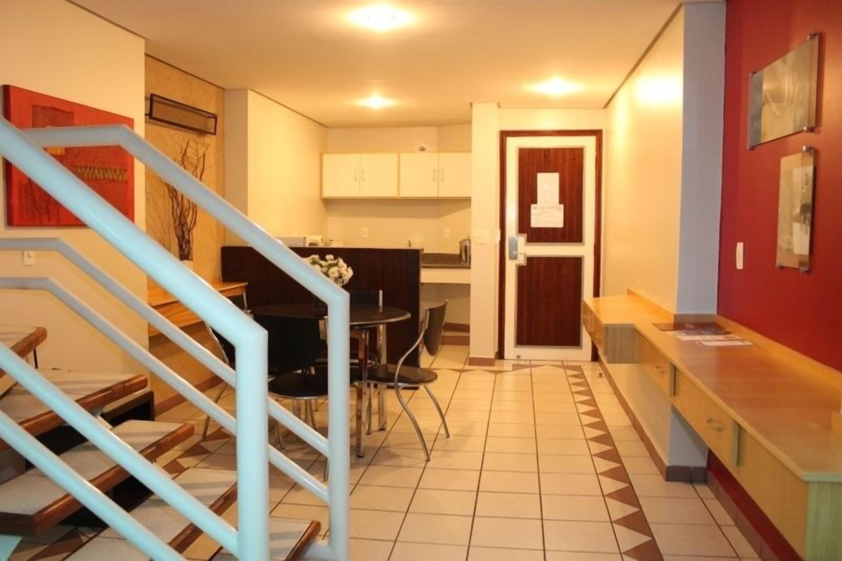 A modern kitchen with white cabinets, a dining area with a black table and chairs, and a staircase with blue railings.