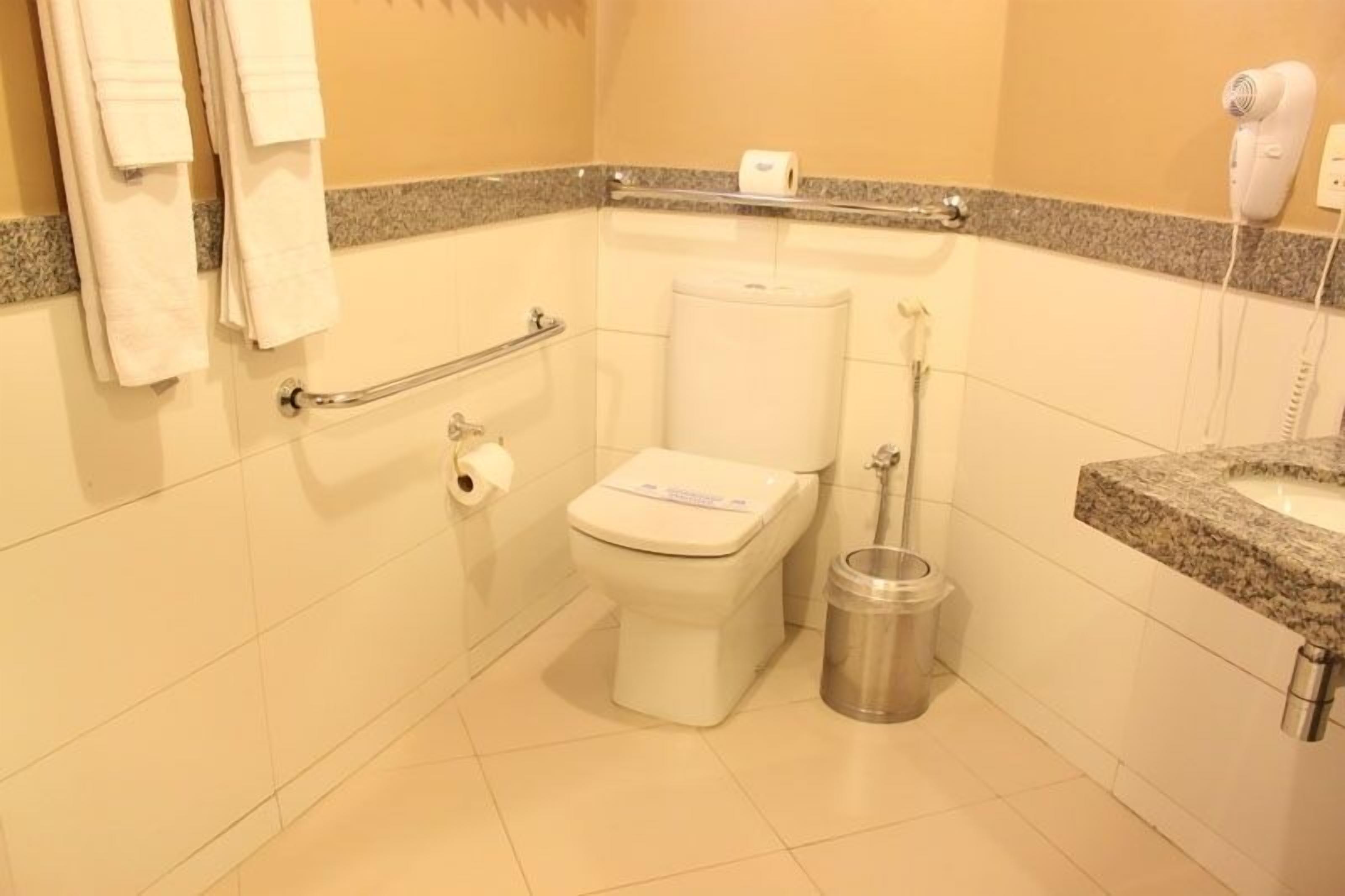 Un baño pequeño con inodoro, secamanos, cubo de basura y toallero.