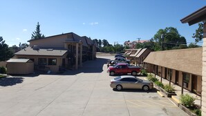 A parking lot with several cars, a building with a sloped roof, and a clear sky. - KC Motel (Show Low)
