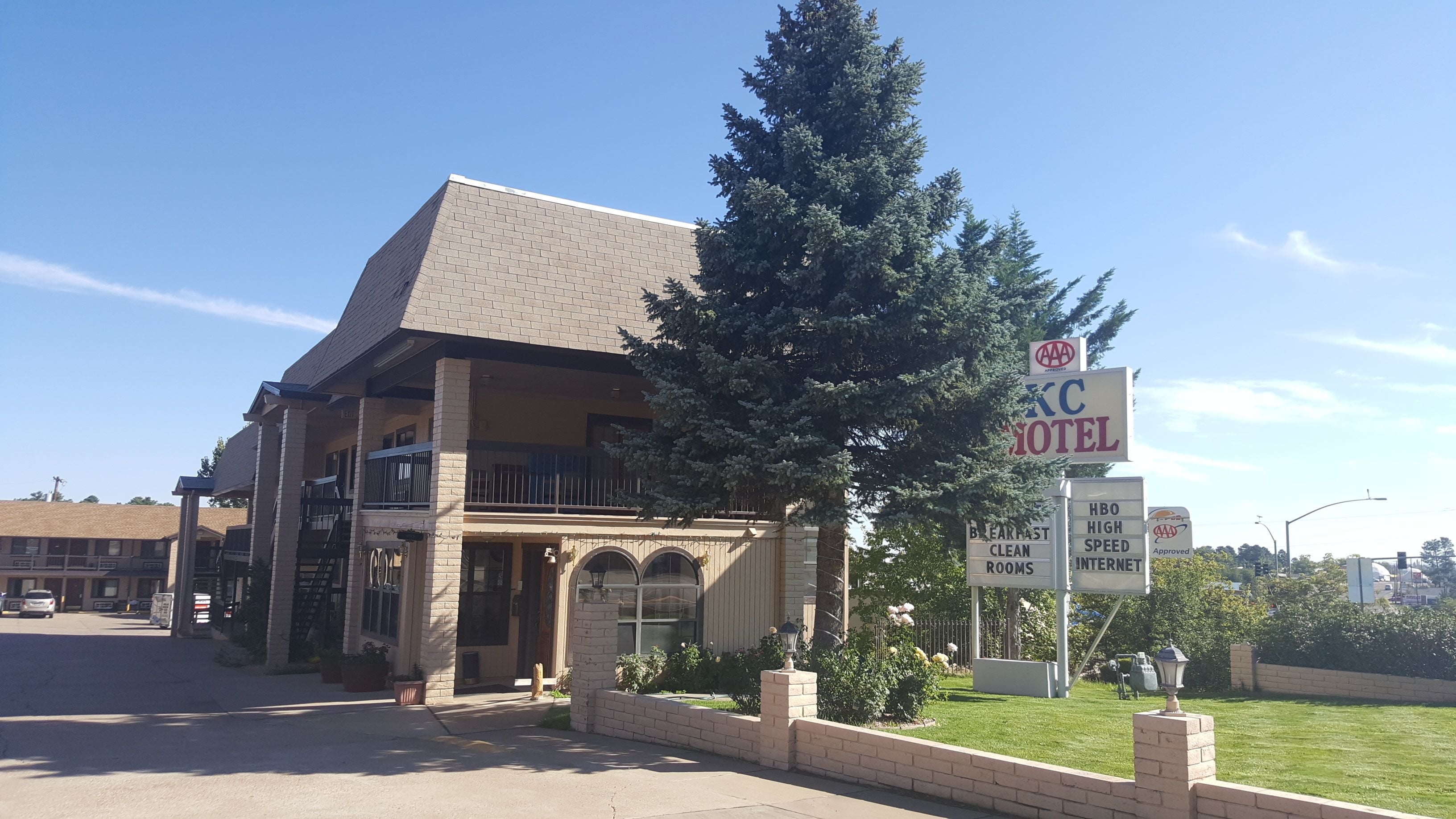 Un hôtel à la façade en briques, avec un grand arbre devant et des panneaux indiquant les services proposés, tels que HBO, une connexion Internet haut débit et des chambres propres.