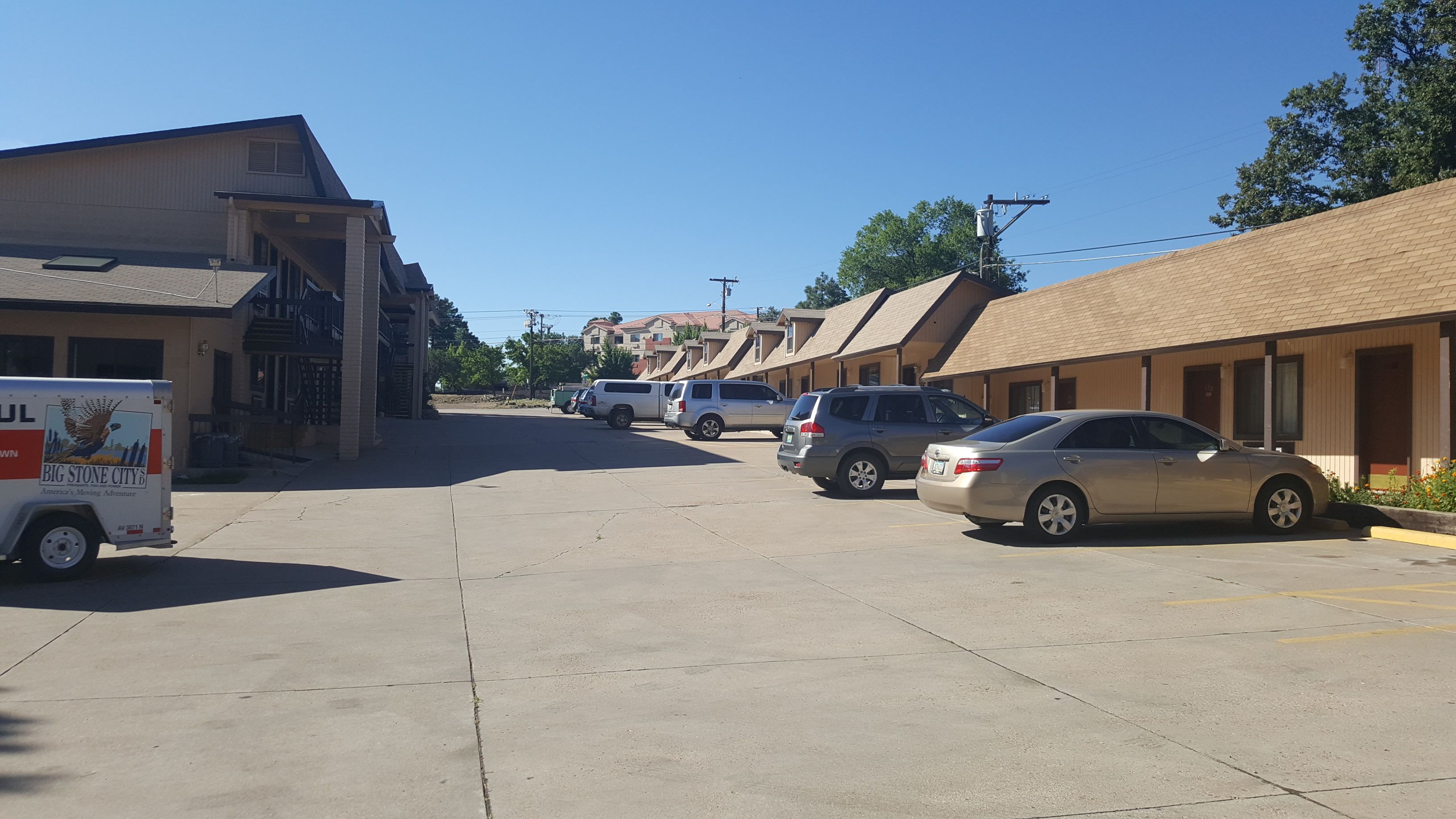 A row of motel buildings with a parking lot in front.