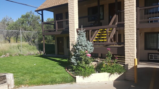 A two-story building with a balcony, a fenced yard, and a small garden with flowers. - KC Motel (Show Low)