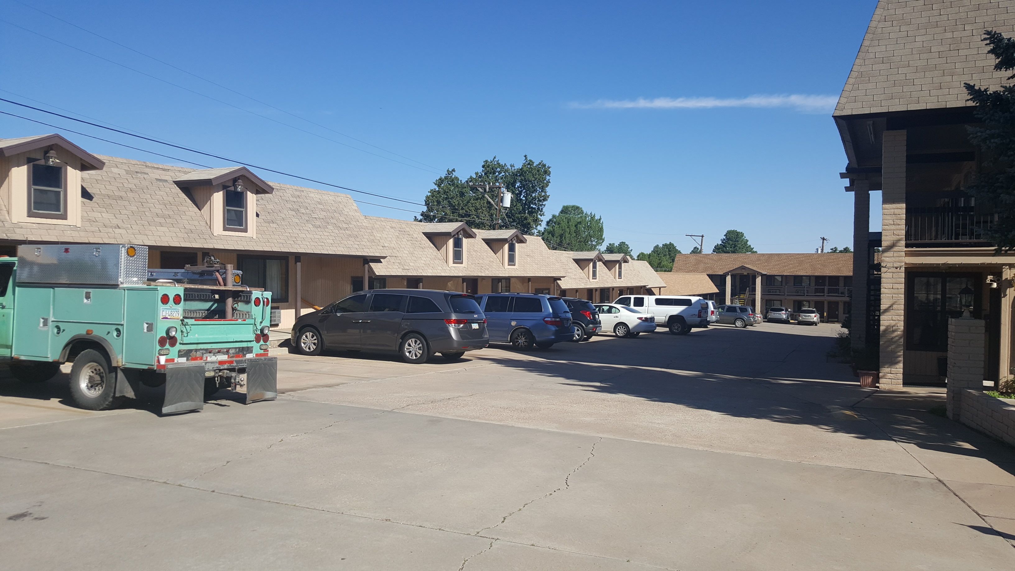 A parking lot with several vehicles, including a utility truck and SUVs, in front of a row of buildings with a simple architectural style.