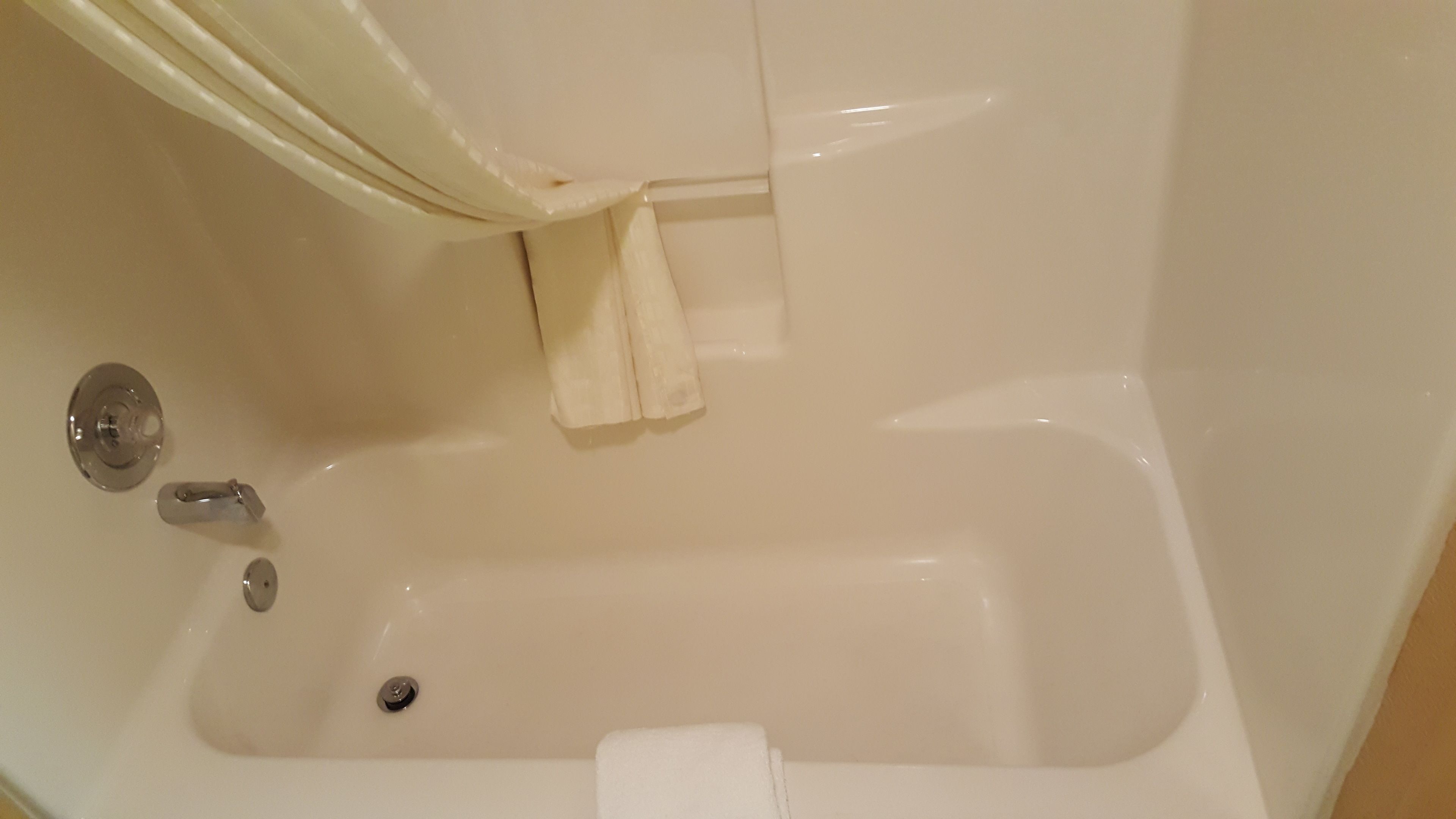 Una bañera blanca con cortina de ducha, grifo y desagüe.