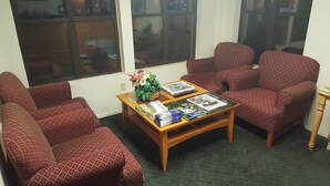 A living room with patterned red sofas, a wooden coffee table with magazines, and a window with reflections. - KC Motel (Show Low)