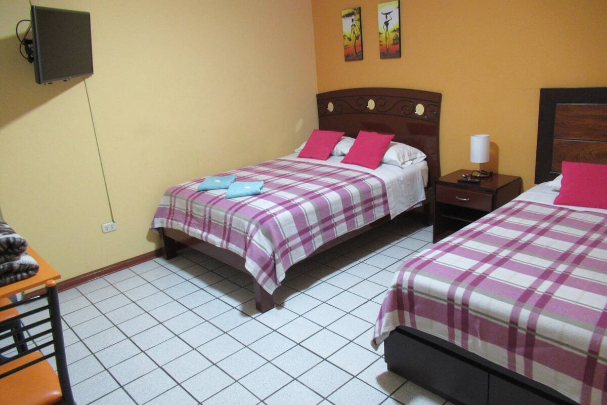 Une chambre d’hôtel avec deux lits, une table de chevet, une chaise et un téléviseur fixé au mur.