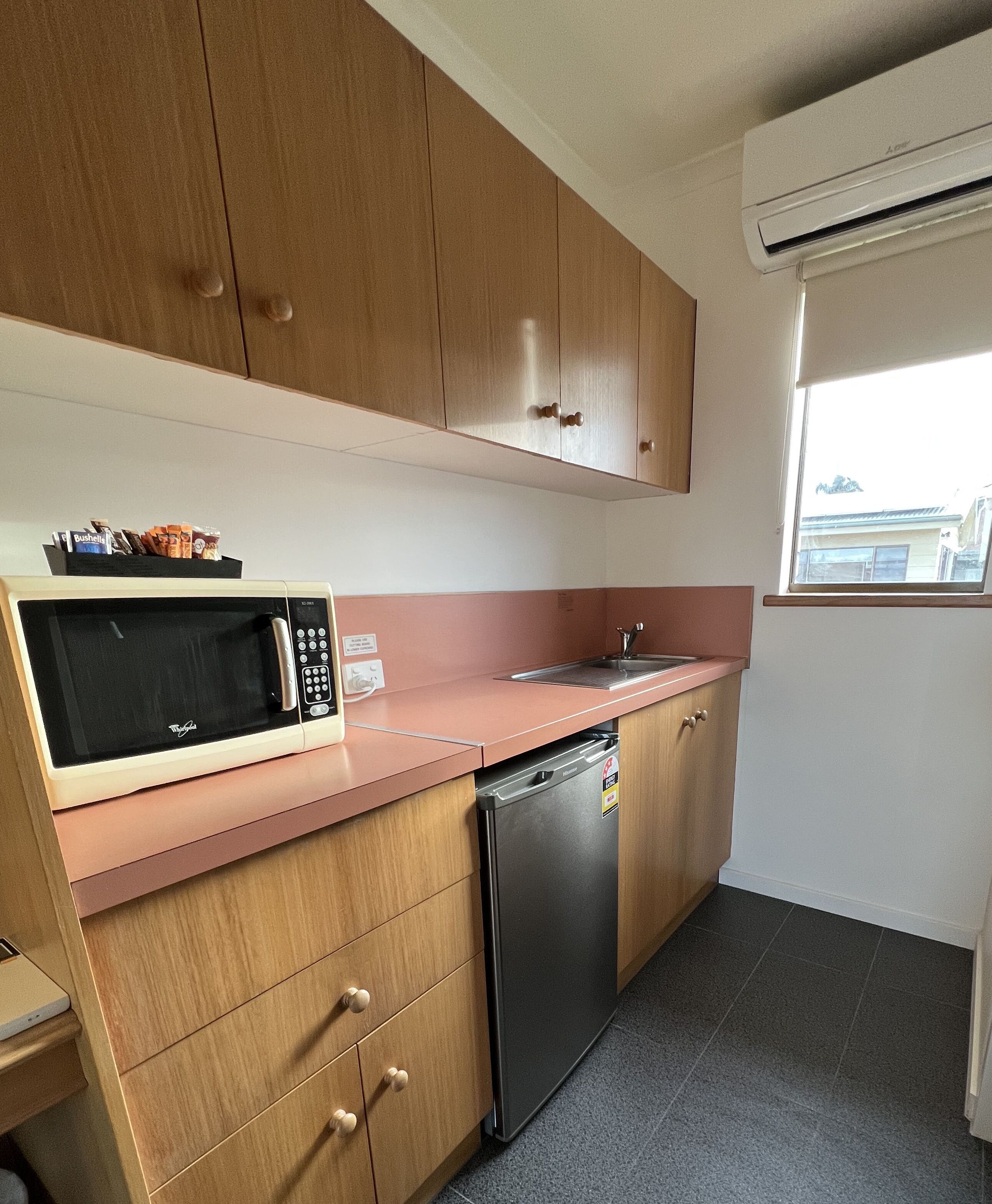 A compact kitchen with wooden cabinets, a microwave, a sink, and a dishwasher.