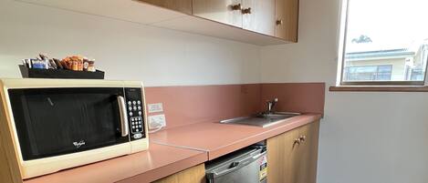 A compact kitchen with wooden cabinets, a microwave, a sink, and a dishwasher.